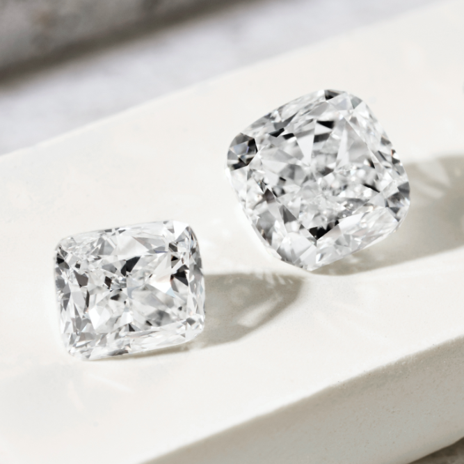 Two cushion-cut diamonds, one bigger than the other, sparkling on a white surface.