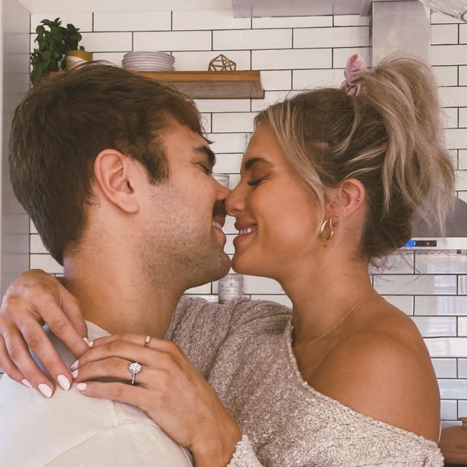 A happy couple sharing an embrace while the woman's hands rest on her partner's shoulder, showing off her diamond engagement ring.